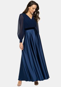 Granatowa satynowa suknia wieczorowa z głębokim dekoltem w kształcie V, przeźroczystymi długimi rękawami, plisowanym body oraz aksamitnym pasaem, spływająca do pełnej spódnicy.