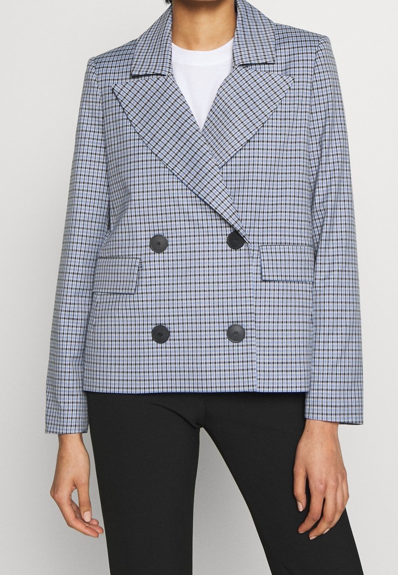 Dubbelsidig kavaj i blå och vit rutig mönster. Har stora svarta knappar och en bred krage. Skräddarsydd passform med sidofickor.