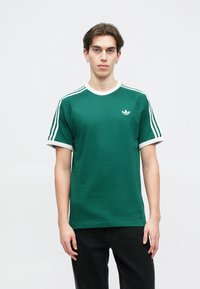 Πράσινη βαμβακερή μπλούζα με άσπρη ραμμένη λαιμόκοψη και μανσέτες, με τρεις άσπρες ρίγες στα μανίκια και κεντημένο λογότυπο στο στήθος.