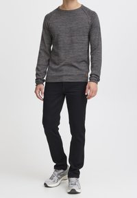 Grau langärmliger Sweatshirt mit strukturiertem Gewebe und rundem Ausschnitt, kombiniert mit schwarzen Jeans und grauen Sneakers. Enthält ein kleines Etikett-Detail.