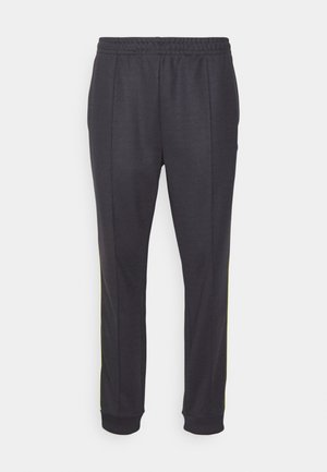 Pantalons de sport noirs en tissu doux. Dotés d'une taille élastique, de jambes fuselées et de rayures jaunes sur les côtés pour l'accent. Texture lisse.