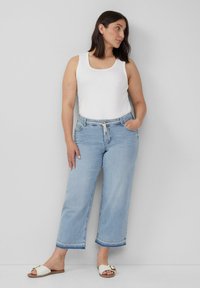 Lichtblauwe relaxte jeans met een rafelige zoom, gecombineerd met een witte tanktop en witte sandalen met een metalen accent.