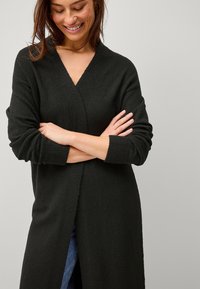 Schwarze Strickjacke mit V-Ausschnitt, langen Ärmeln und einer offenen Vorderseite. Der Stoff ist weich und leicht strukturiert. Sie hat einen lässigen Schnitt.