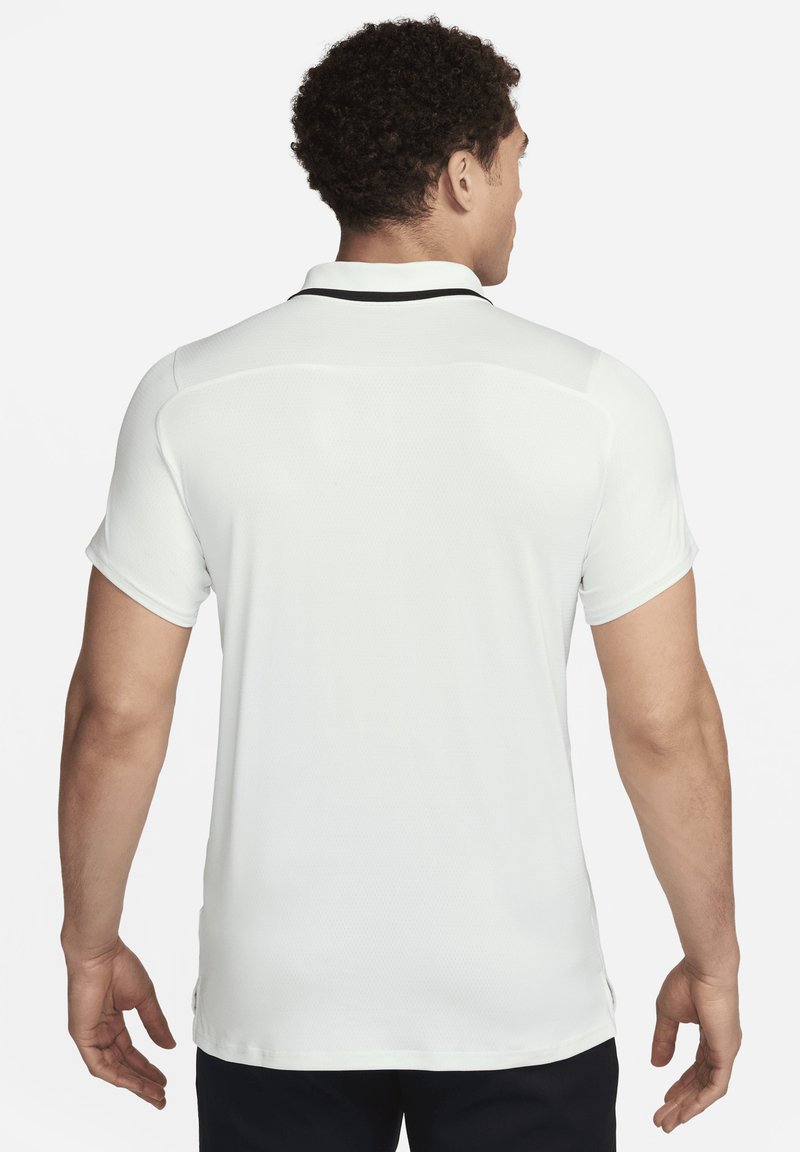 Camiseta polo blanca con tejido texturizado, mangas cortas y un acento negro en el cuello. La camiseta tiene un corte relajado y aberturas laterales.