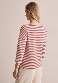 Suéter de punto a rayas rojas y crema con mangas tres cuartos y un escote redondeado, que presenta un patrón texturizado.
