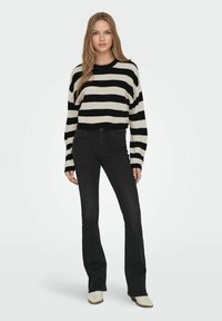 Maglione a righe nero e crema, lavorato a maglia, con maniche lunghe e vestibilità corta, abbinato a jeans neri a zampa d'elefante e stivaletti leggeri.