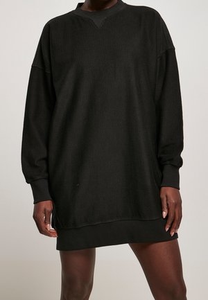 Robe noire à côtes surdimensionnée avec des manches longues, décolleté en V et poignets. Texture douce, atteignant le milieu de la cuisse, conçue pour le confort et la facilité.