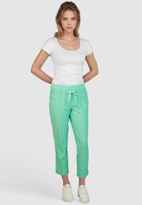 Minzgrüne Jogginghose mit elastischem Bund und Kordelzug. Getragen mit einem weißen, figurbetonten T-Shirt und weißen Sneakers. Glattes, leichtes Material.