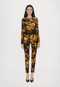 Top a maniche lunghe nero e oro e pantaloni attillati con un elaborato motivo floreale. Il tessuto appare liscio con un leggero lucido.