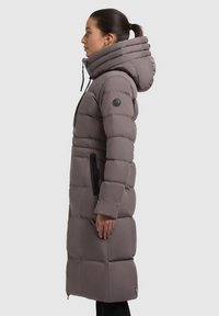 Lang quilted frakke i grå, med høj krave, lynlåslommer, ribbede detaljer og hætte. Polstret design til isolering.