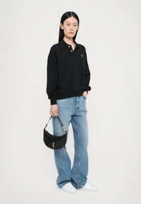 Schwarzes Polo-Sweatshirt mit Kragen und kleinem Logo, kombiniert mit hellblauen Jeans und weißen Sneakers. Schwarze Umhängetasche mit goldenen Akzenten.