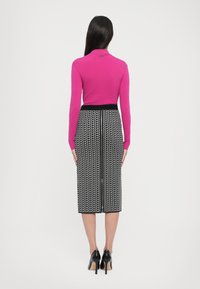 Figurbetontes pinkes Sweatshirt mit hohem Kragen und einem Bleistiftrock mit schwarz-weißen Muster. Schwarze High Heels runden das Outfit ab.
