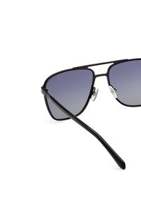 Gafas de sol aviador negras con lentes degradados, marco de metal delgado y almohadillas de silicona en la nariz. Presenta un diseño elegante y angular con patillas rectas.