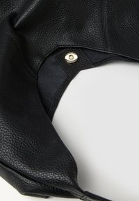 Borsa a tracolla in pelle nera con una superficie testurizzata, dotata di una chiusura a scatto dorata. Il design è minimalista con bordi morbidi e curvi.
