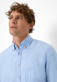 Light blue button-up shirt made of textured fabric with a pocket. Features a classic collar and thin, neutral buttons.