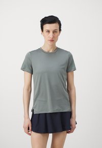 Olīvu zaļš sporta krekls ar īsām piedurknēm, apaļu kakla izgriezumu un sānu iedaļām. Apvienots ar tumši zilu svārku ar šortiem. Gluda, viegla auduma.