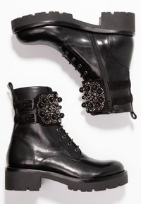 Stivaletti neri in pelle con suola in gomma spessa. Presentano un cinturino decorativo con delle perle nere e strass, cerniera e design con lacci.