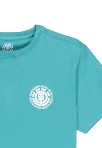 Tyrkysové bavlnené tričko s bielym kruhovým logom, na ktorom sú slová "Zem, Vietor, Oheň, Voda" a centrálna grafika stromu.