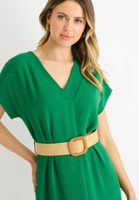 Abito verde a collo a V realizzato in tessuto leggero, con maniche corte e vita cinchata adornata da una cintura intrecciata beige con dettaglio della fibbia quadrata.