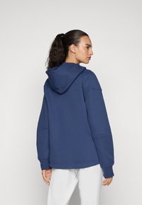 Navy blue hoodie with a front kangaroo pocket, drawstring hood, and ribbed cuffs. Soft fabric with a loose fit and minimal seams.