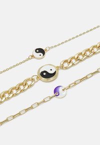 Pulseiras em tom dourado com símbolos Yin-Yang, duas com esmalte preto e branco e uma com detalhes em roxo, exibindo vários estilos de corrente.