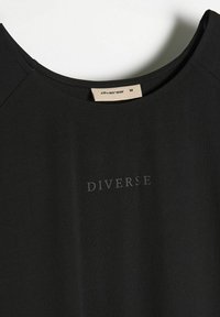 Czarny bawełniany t-shirt z okrągłym dekoltem, z subtelnym szarym napisem "DIVERSE". Metka z neutralnego materiału przy kołnierzyku.