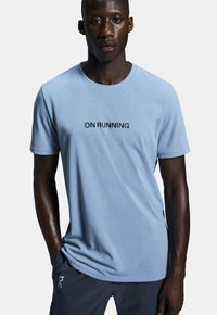 Light blue short-sleeve t-shirt made of soft fabric, featuring a black "ON RUNNING" print across the chest. Smooth texture and relaxed fit.