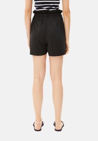 Black shorts with a gathered waistline, smooth texture, and a loose fit, paired with black flip-flops and a pink ankle bracelet.