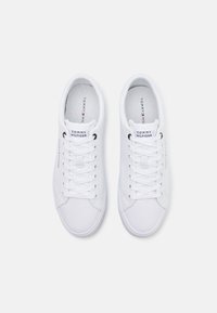 Baskets en toile blanches avec bout rond, lacets plats et détail de logo discret sur la languette. Surface texturée et design minimaliste.