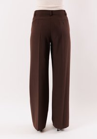 Pantaloni marroni a gamba larga con un design sartoriale, passanti per cintura e pieghe sul davanti. Tessuto liscio adatto all'abbigliamento formale.