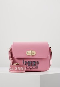 Lyserød syntetisk læder crossbody taske med magnetisk lukning, guld hardware og tekstureret logo design. Inkluderer en aftagelig rem.