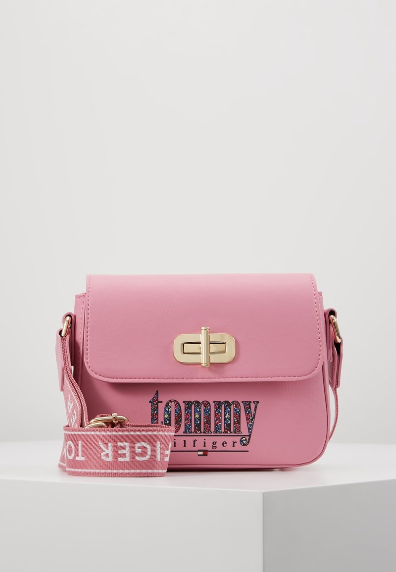 Lyserød syntetisk læder crossbody taske med magnetisk lukning, guld hardware og tekstureret logo design. Inkluderer en aftagelig rem.