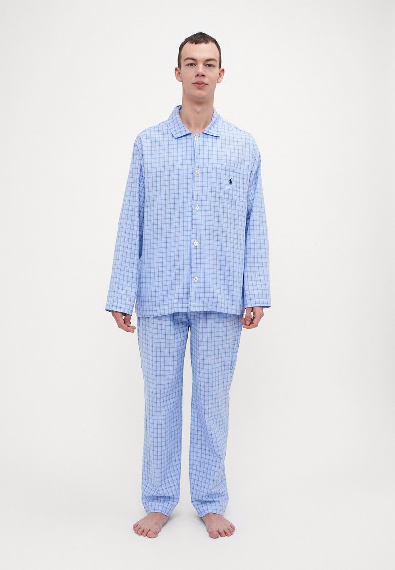 Ensemble de pyjama à carreaux bleus avec des manches longues, fermeture à boutons à l'avant et une poche sur la chemise. Le pantalon présente des carreaux assortis. Texture de tissu douce.