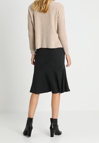 Vaaleanruskea ribbineulepusero, jossa pitkät hihat, yhdistetty tummanharmaaseen kellohameeseen. Asun täydentävät mustat nilkkurit, joissa on korko.