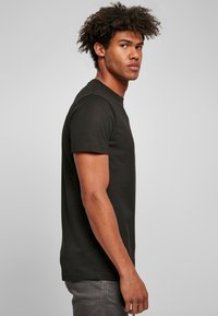 Tricou negru cu mânecă scurtă, fabricat din bumbac, cu decolteu rotund și croială clasică, prezentat pe un model din lateral.