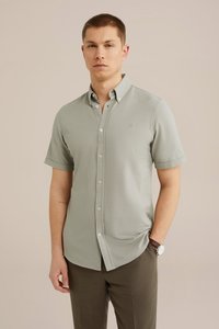 Camicetta a maniche corte, di un grigio chiaro, con bottoni, realizzata in un tessuto morbido, dotata di colletto, logo di marca e vestibilità slim, indossata con pantaloni marroni.