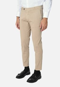 Chino beige con una vestibilità slim e frontale piatto, dotati di una chiusura con un solo bottone e passanti per cintura. Indossati con mocassini neri e calzini.