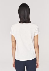 Camiseta de algodón blanca con un corte relajado, mangas cortas y cuello redondo. La parte de atrás presenta una pequeña etiqueta de la marca cerca del cuello.
