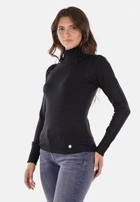 Maglione a collo alto nero a maniche lunghe con dettagli a coste e un piccolo logo metallico in vita. Texture liscia e design aderente.
