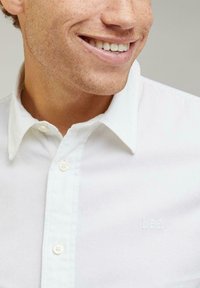 Chemise blanche à boutons avec une texture douce et un col pointu. Présente une broderie discrète "Lee" sur la poitrine.