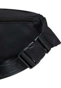 Detail van een zwarte stoffen tas met een ritsluiting, textuurriem en plastic gesp met een logo. Het materiaal lijkt duurzaam en utilitair.