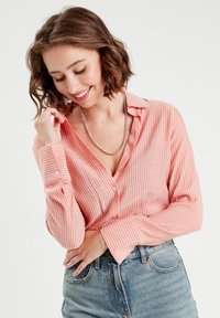 Chemise boutonnée à manches longues rayée en corail clair avec des lignes blanches, présentant un col en V, des manches à revers et une coupe décontractée.