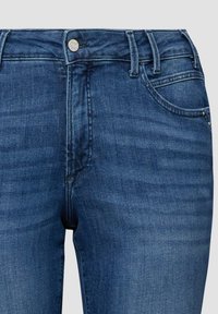 Dunkelblaue Denim-Jeans in Vorderansicht mit Knopfverschluss, Gürtelschlaufen und Vordertaschen, dargestellt vor neutralem Hintergrund.