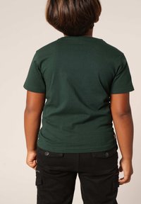 Donkergroen katoenen t-shirt met korte mouwen en een ronde hals, gecombineerd met zwarte cargo-broeken met zijzakken en knoopdetails.