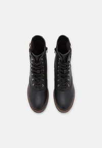 Botas de tobillo de cuero negro con una textura suave, que cuentan con ojales dorados, cordones y una cremallera lateral, además de una suela de goma marrón.