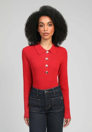 Haut rouge à manches longues côtelé avec un col et cinq boutons décoratifs, associé à un jean en denim foncé taille haute avec deux poches arrière.