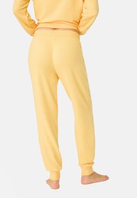 Pantaloni jogger giallo chiaro con una texture morbida, vita elastica e polsini, caratterizzati da un fit rilassato e senza motivi o hardware visibili.