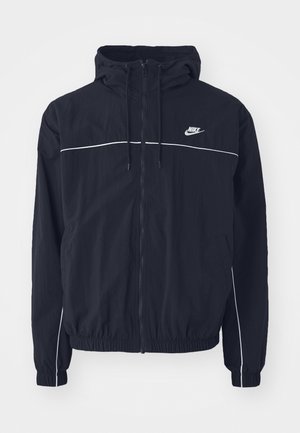 Giacca nera con cappuccio Nike con cerniera frontale completa, piping bianco su petto e maniche, polsini elastici e tasche laterali.