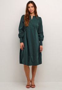 Türkises Kleid aus glattem Stoff, mit V-Ausschnitt, langen puffärmel und gerafftem Saum. Klassische A-Linie Silhouette.