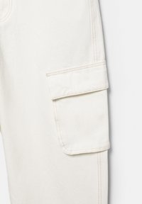 Krémové cargo nohavice s klopovým vreckom na stehne, viditeľným prešitím a textúrovanou látkou.